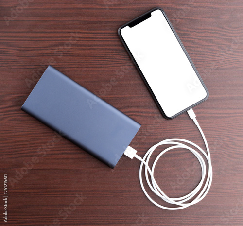 Power bank and smartphone on wooden table. The smartphone is charging from the power bank. photo