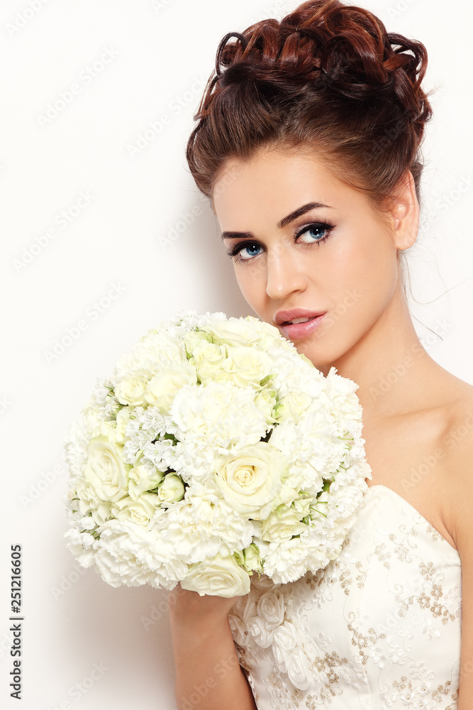 Young beautiful happy bride with winged eye make-up and prom hairdo holding fancy bouquet in her hand Young beautiful happy bride with winged eye make-up and prom hairdo holding fancy bouquet in her hand