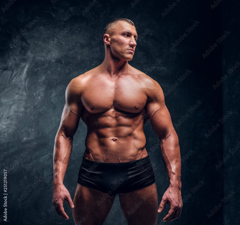 A handsome athletic man with perfect pumped body wearing underwear. Studio photo with dark wall background 
