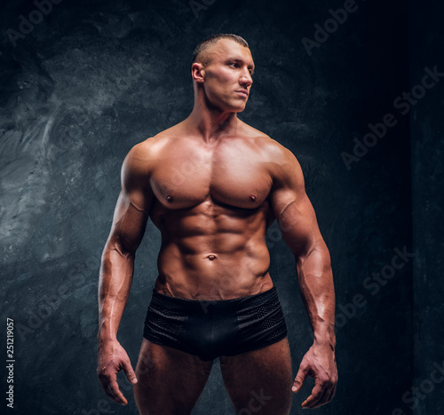 A handsome athletic man with perfect pumped body wearing underwear. Studio photo with dark wall background  © Fxquadro