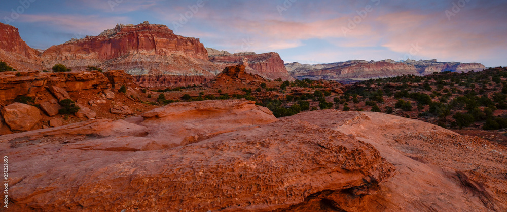 Sunset during golden hour in Southern Utah, sun warming red sandstone, cliffs, mountains, and mesa.  with light blue sky and pink clouds