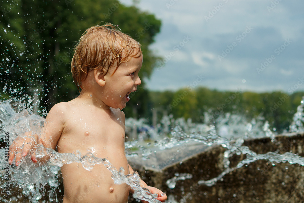 Funny baby boy trying to cauch water stream in fountain. Cute toddler playing in the city fountain Funny baby boy trying to cauch water stream in fountain. Cute toddler playing in the city fountain