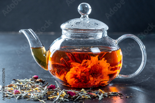 Tea in a glass teapot with a blooming large flower. Teapot with exotic green tea-balls blooms flower and dried tea and rose buds photo