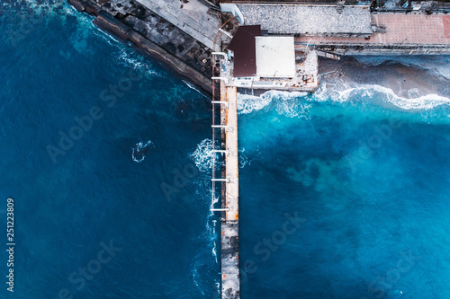 Aerial top view of concrete pier or breakwater in bright blue sea water with waves near coastline, abstract ocean travel vacation background © DedMityay