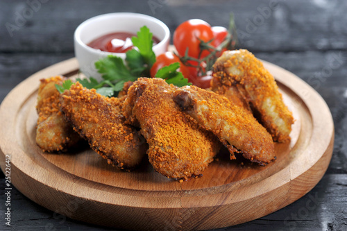 Chicken wings with crispy crust. The composition is complemented by cherry tomatoes, parsley and a chachka with ketchup sauce. Dark wooden background. Close-up. 