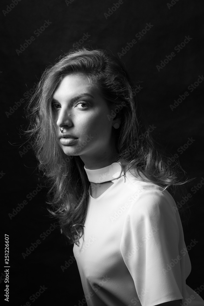 Black and white fashion portrait of beautiful model woman with luxurious curly hair in elegant white blouse posing in studio in front of black background. Art photo portrait