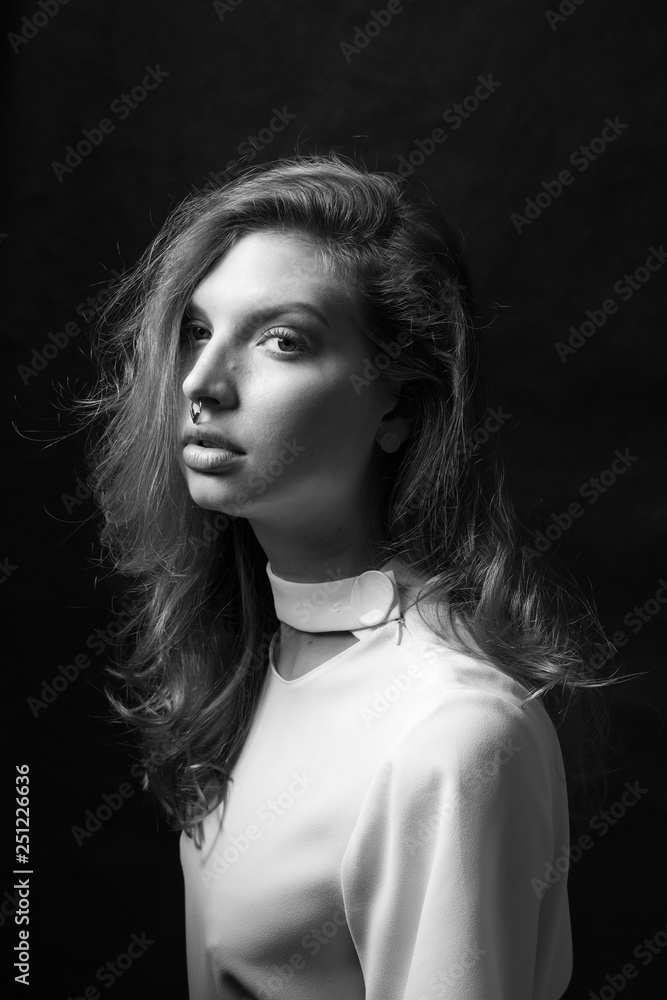 Black and white fashion portrait of beautiful model woman with luxurious curly hair in elegant white blouse posing in studio in front of black background. Art photo portrait