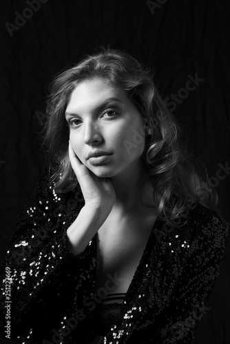 Portrait of beautiful sexy woman with luxurious curly hair in elegant black jacket with rhinestones posing in studio. Black and white vogue portrait