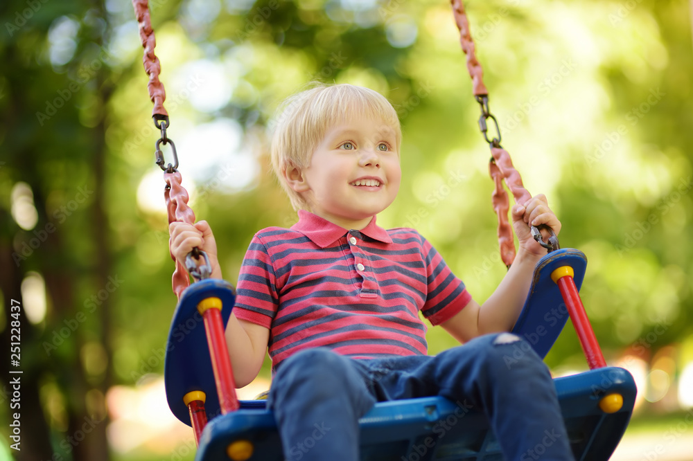 Cute little boy having fun on outdoor playground. Child on swing