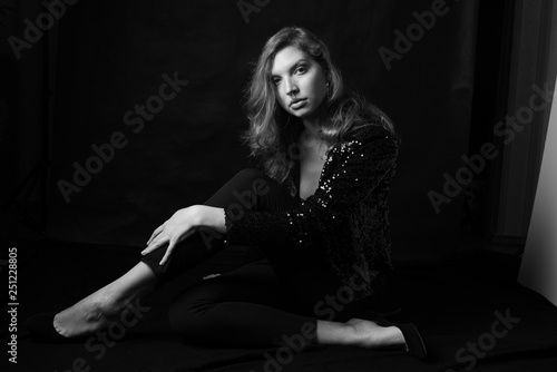 Black and white fashion photo of beautiful sexy woman with luxurious curly hair in elegant jacket with rhinestones posing in studio in front of black backgroung. Full-length girl model
