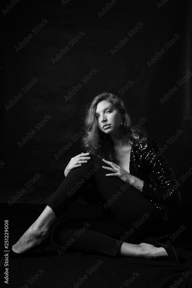 Black and white fashion photo of beautiful sexy woman with luxurious curly hair in elegant jacket with rhinestones posing in studio in front of black backgroung. Full-length girl model Black and white fashion photo of beautiful sexy woman with luxurious curly hair in elegant jacket with rhinestones posing in studio in front of black backgroung. Full-length girl model