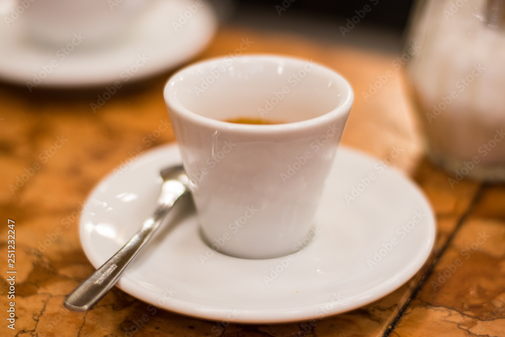 White Espresso Coffee Cup On A White Saucer With A Spoon On Table. White Espresso Coffee Cup On A White Saucer With A Spoon On Table.