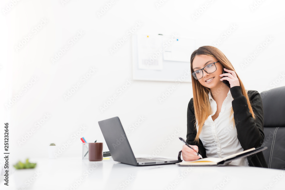 Smiling beautiful business woman talking on smartphone while taking a notes. Smiling beautiful business woman talking on smartphone while taking a notes.