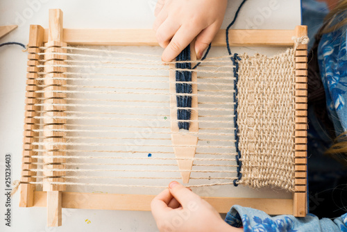 A little girl learns process to weave thick threads. Hands close up.