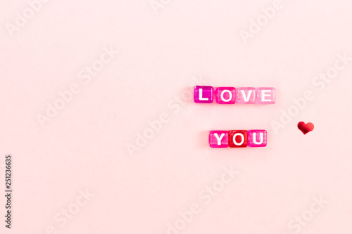 Love you inscription made of colorful cube beads with letters. Festive pink background concept with copy space