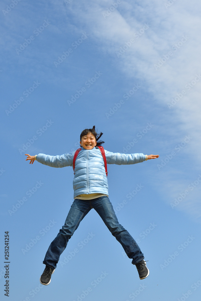 青空でジャンプする女の子（ランドセル）