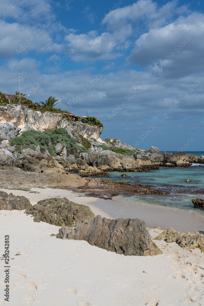 coastline in Cozumel Mexico with rocky cliff, turquoise water of the Caribbean, blue sky with puffy clouds and  white sand beach