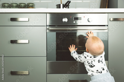 Little child playing with electric stove in the kitchen. Baby safety in kitchen photo