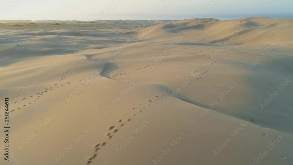 Aerial pan across sand dunes and footprints trails at sunrise Aerial pan across sand dunes and footprints trails at sunrise