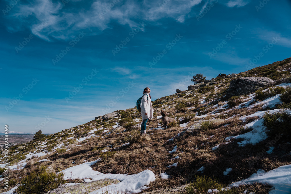 Young backpacker enjoying a sunny winter day in the mountains. Breathing fresh air, relaxed and carefree. Some snow all around. Amazing view. Lifestyle.