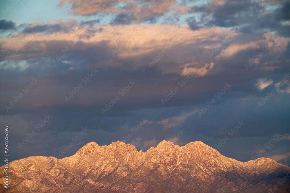 Snow covered mountains glow at sunset under dramatic sky 