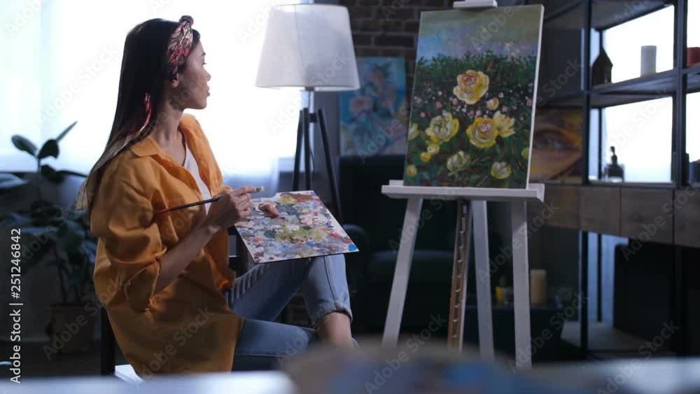 Side view of female painter holding palette and sitting near her ...