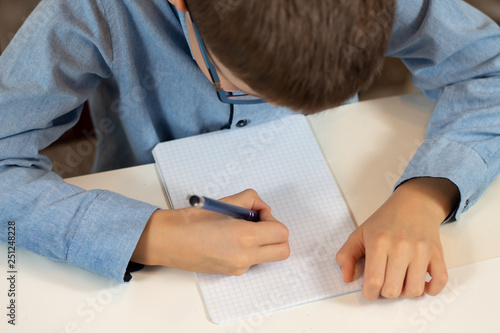 Chłopiec siedzi przy biurku z długopisem w dłoni i pisze w zeszycie.