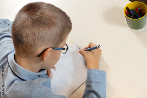 Chłopiec uczy się pisać litery. Dłonie chłopca trzymają długopis. Pisanie liter w zeszycie.
