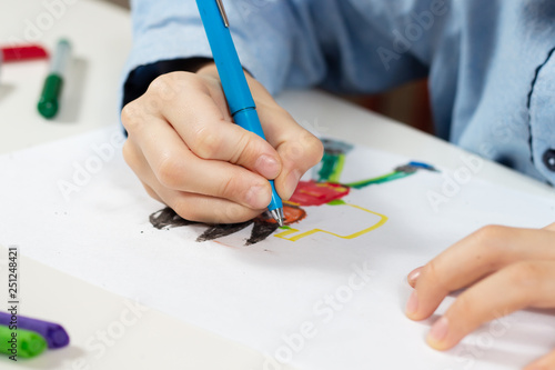 Dłonie dziecka trzymają długopis i rysują wymyśloną postać na białej kartce papieru.