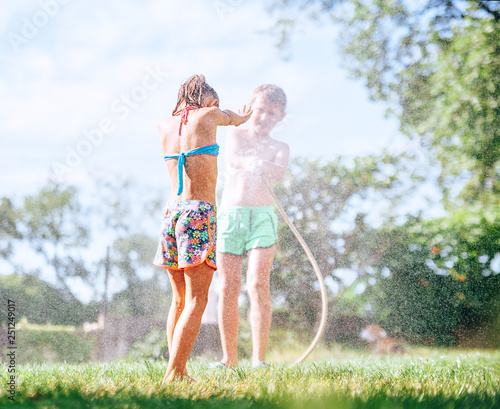 Two kids playing at garden, pours each other from the hose, makes a rain