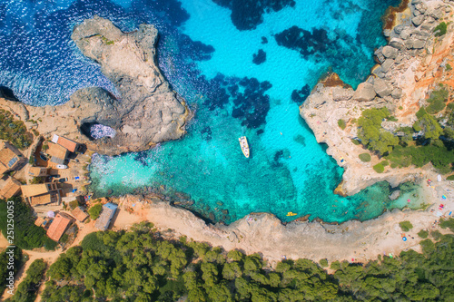Aerial view of clear sea with blue water, sandy beach, rocks, green trees, yachts and boats in sunny morning in summer. Travel in Mallorca, Balearic islands, Spain. Top view. Colorful landscape