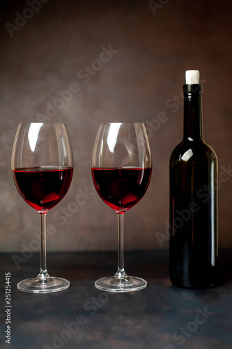 Glasses with red wine and a bottle on a stone background.