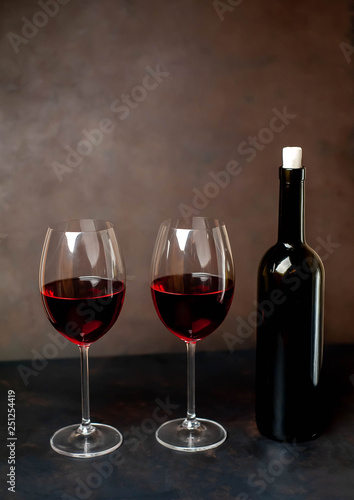 Glasses with red wine and a bottle on a stone background.