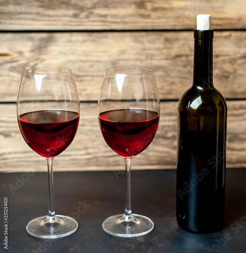 glasses with red wine and a bottle on a background of stone and wood