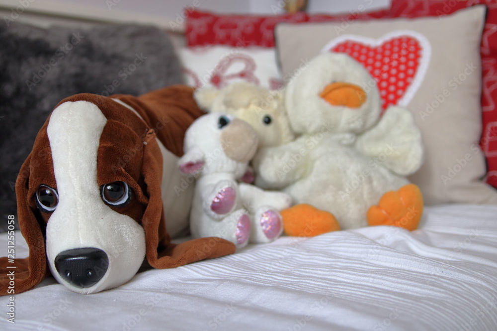 Plush toys like dog, sheep, duck lie down on couch covered with white blanket, in background colorful decorative pillows