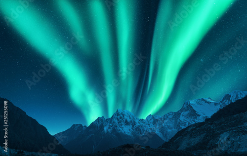 Aurora borealis above snow covered mountain range in europe. Northern lights in winter. Night landscape with green polar lights and snowy mountains. Starry sky with aurora. Nature background. Space