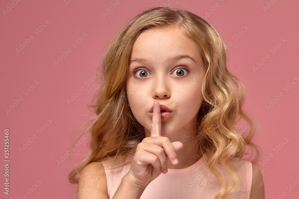 Little girl with a blond curly hair, in a pink dress is posing for the camera Little girl with a blond curly hair, in a pink dress is posing for the camera