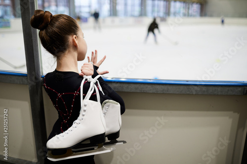 Canvas Print Back view portrait of future figure skater standing by ice rink and watching tra