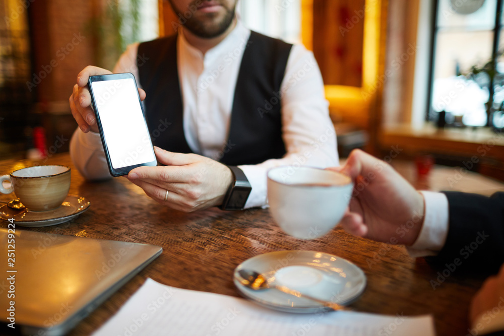 Fototapeta premium Closeup of unrecognizable businessman showing smartphone with blank screen during meeting in cafe, copy space