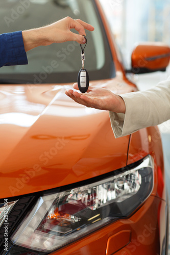 Dealer giving key to new owner at orange jeep on background.