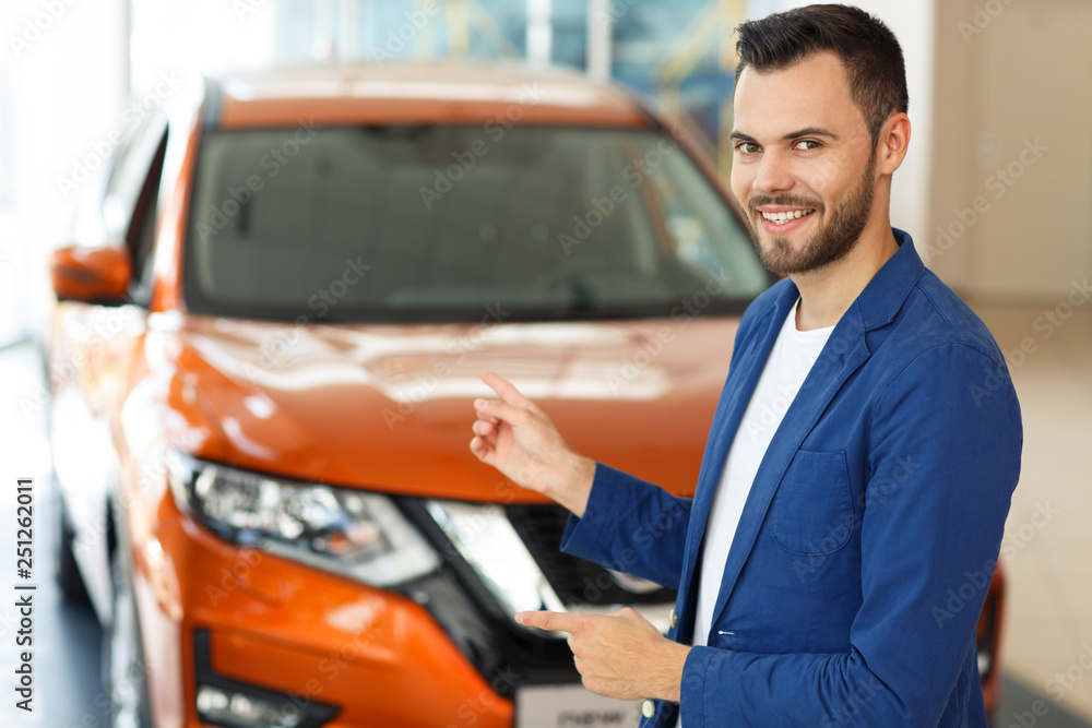 Bearded man pointing by hand at orange jeep behind him.