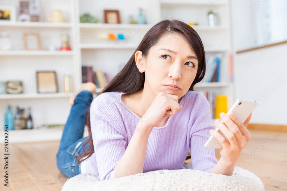 部屋でスマホを見る女性　考える