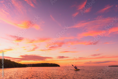 Kayaker man kayaking sea kayak at sunset on summer ocean nature landscape. Amazing scenery with pink colored sky.