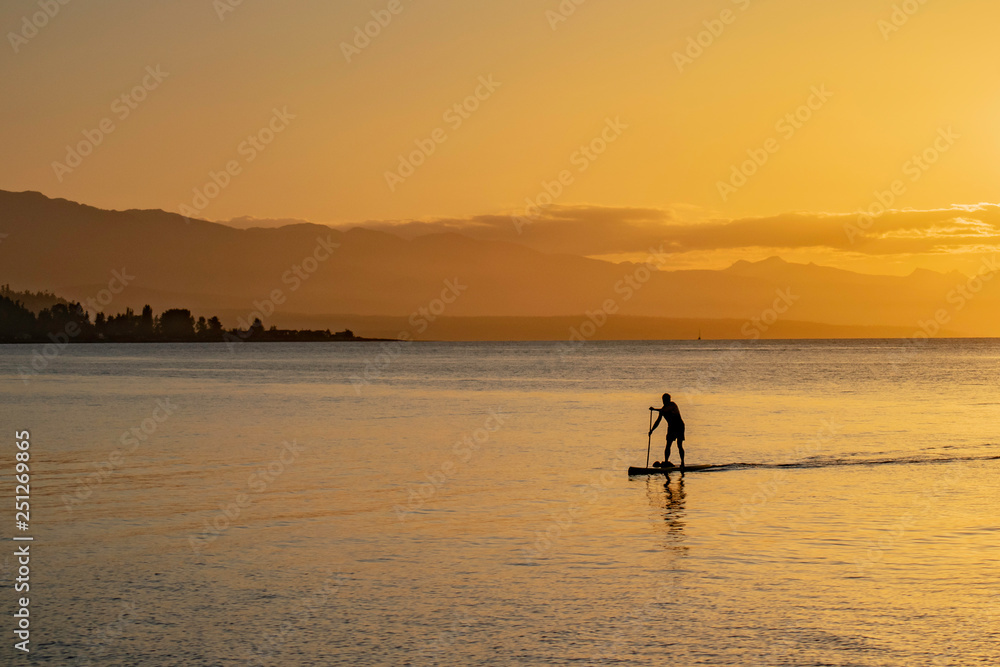 Silhouette Of A Man Paddleboarding Into Shore At Sunset