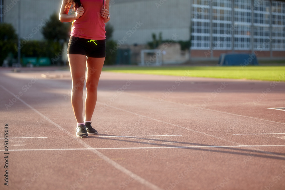 one young woman, unrecognizable person, wearing fitness clothes, walking on a sports court. On a track and field, running tracks.