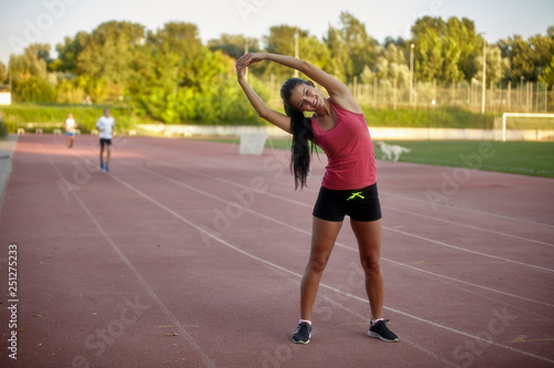 one young happy, smiling woman, stretching upper body - arms, leaning to one side. On a stadium, track and field stadium.