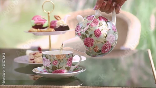 Woman's hand pouring green tea from a beautiful teapot into a tea cup with window light in background.