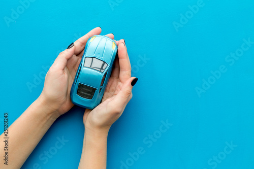 Car insurance concept. Safety of auto. Car toy in female hands on blue background top view copy space