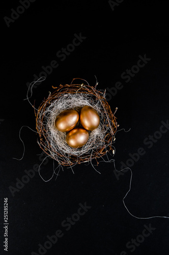 Golden Easter Eggs in birds Nest on black background. Easter Holiday concept abstract background copyspace top view several objects.