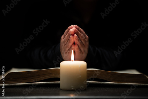 Tableau sur toile Person Praying with Hands Over Bible Illuminated by Candle Light